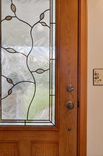 An attractive, steel entry door, manufactured by Pella, has a leaded glass window pane allowing sunny daylight to stream in from the East.