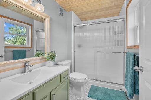 Primary bathroom with stylish and updated vanity, tiled floors, wood accent ceiling and a window.