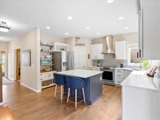 Updated kitchen featuring rich wood floors, stainless steel appliances, quartz countertops, and a walk-in pantry.