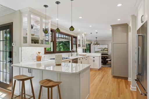 Bright and modern kitchen showcases spacious work surfaces, plenty of storage, and a beautiful backsplash accented by chic pendant lights