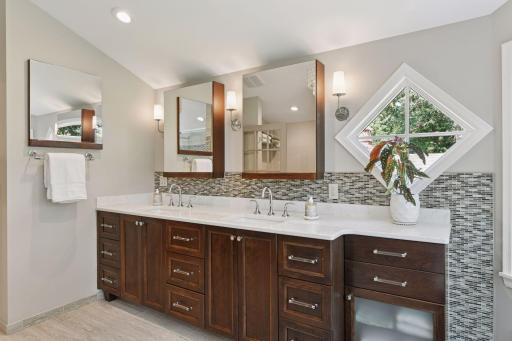 Modern double vanity featuring rich wood cabinetry and designer lighting. A diamond-shaped window and lush views add a touch of natural serenity to this spa-like space