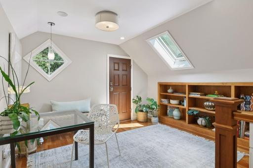 Bright and versatile upper-level loft showcases a custom wood bookcase, abundant windows, and convenient access to a large walk-in attic