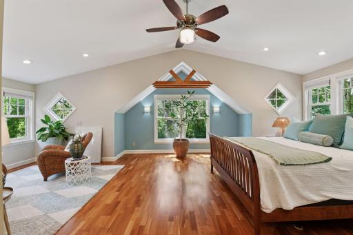 Spacious primary bedroom with vaulted ceilings, rich hardwood floors, cozy seating area, and abundant natural light from multiple windows
