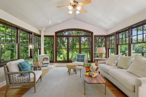 Spacious cantilevered sunroom with vaulted ceilings, heated floors, and Jotul fireplace surrounded by windows offering serene views of the backyard and creek beyond