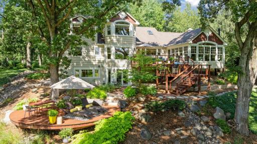 Expansive tiered deck with dedicated dining and lounging areas overlooks a lush green backyard, framed by large windows that flood the home with natural light