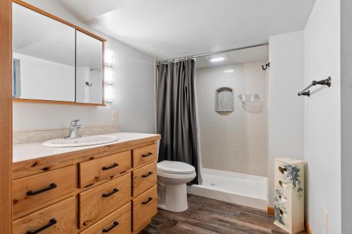 Upper level 3/4 bath boasts a warm wooden vanity, LVP flooring, and a beautifully tiled shower.