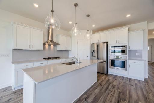 (Photo of a decorated model, actual homes finishes will vary) This gourmet kitchen offers a walk-in pantry, stainless steel appliances, LVP flooring, quartz countertops, white cabinetry and more!