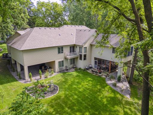 This home's gorgeous rear exterior view and backyard features manicured landscaping, mature trees, and multiple seating areas—perfect for quiet relaxation or entertaining. The screen porch walkout opens to a serene green space and stone patios.