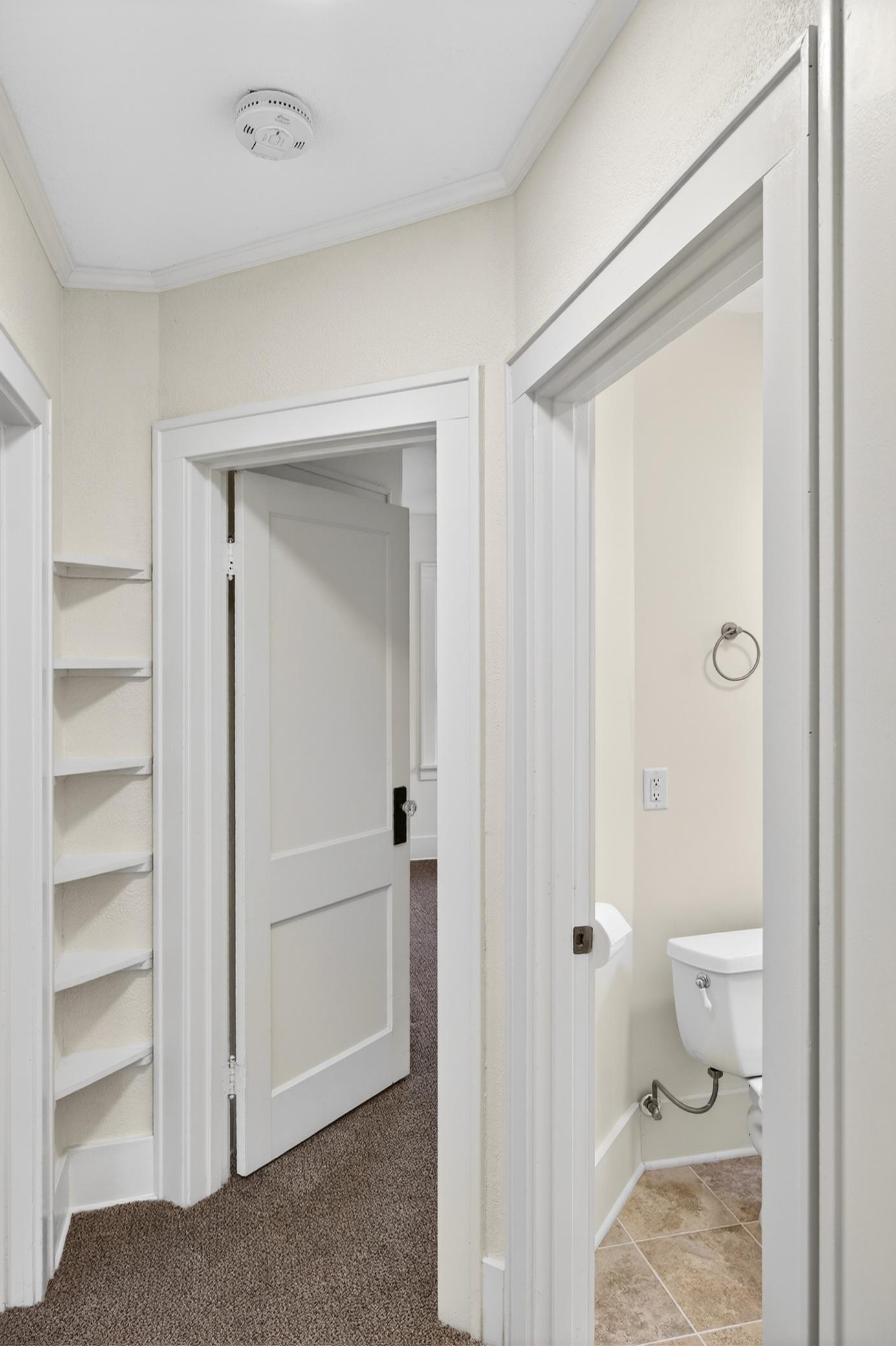 Hallway with six corner shelves, new carpeting, and access to the bathroom and the 2nd bedroom.