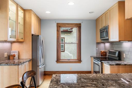 Bright kitchen with sleek granite countertops, stainless appliances, and custom glass-front lighted cabinet