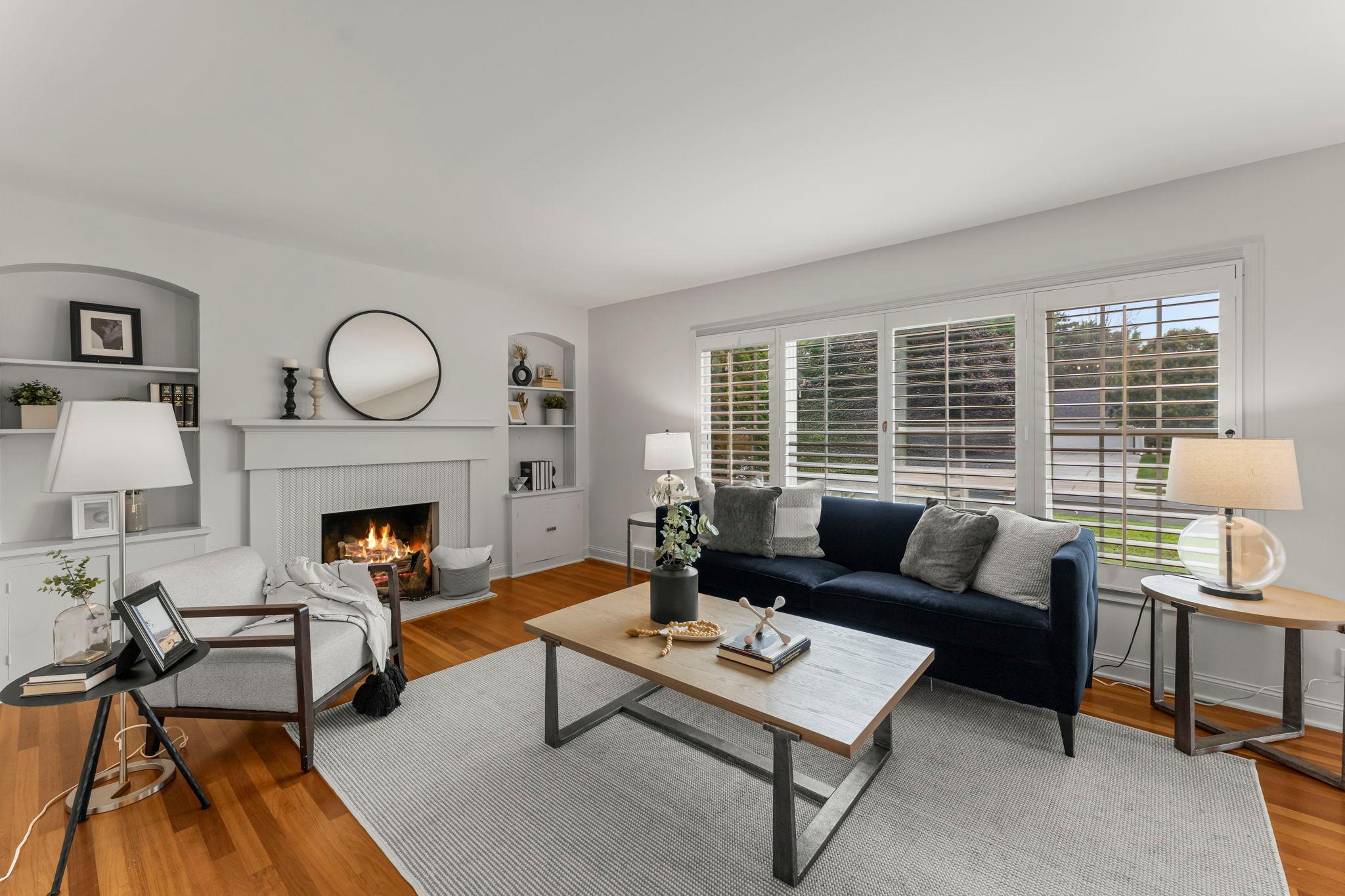 The living room feels cozy yet spacious with its large windows, wood-burning fireplace, and built-in shelving and cabinetry.