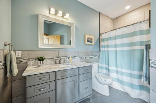 Stylish main-level bath featuring a marble-topped vanity, custom tilework, and soft blue accentsâoffering both function and charm for guests and everyday use.