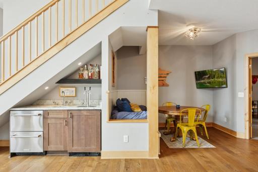 Sleek wet bar tucked beneath the staircase features a built-in kegerator, beverage drawers, and open shelvingâperfect for entertaining with style and ease.