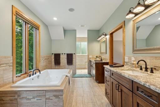 Spa-like primary bath featuring a soaking tub, heated floors, dual vanities with granite tops, and a spacious walk-in tiled shower.