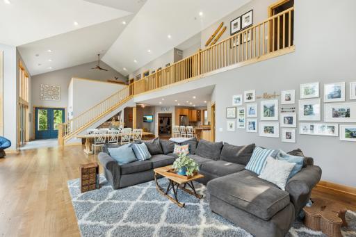 Expansive great room with soaring ceilings, white oak floors, and a dramatic open staircase. Natural light pours in through a wall of windows, creating the perfect space to gather and relax.