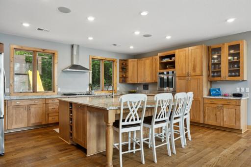 Chefâs kitchen boasts a sprawling center island with seating, rich white oak flooring, stainless appliances, and custom cabinetry that blends warmth with timeless elegance.