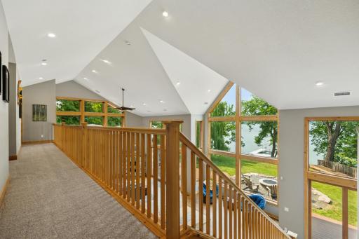 Upper-level walkway overlooks the stunning great room below and captures breathtaking lake views through soaring windowsâan architectural showpiece that connects both levels with style.
