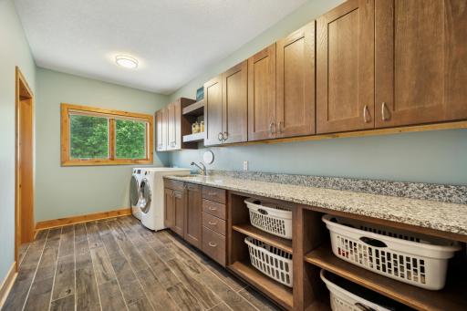 Spacious upper-level laundry room featuring abundant cabinetry, granite folding counter, and walk-in storage closet for ultimate organization.