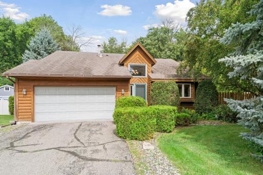 Charming wood-paneled exterior with mature landscaping and a two-car garage. A peaceful setting surrounded by lush greenery and trees.