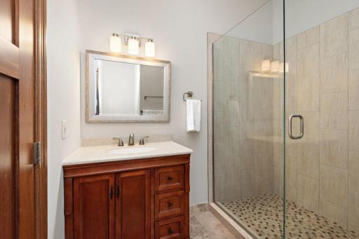 Both main floor bedrooms offer custom closets and junior ensuite baths, featuring walk-in showers dressed in frameless glass, w/ man made stone accents.