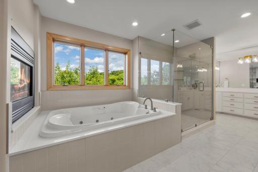 The luxurious en suite bathroom offers a spa-like experience with elegant tile flooring, a large jetted soaking tub, a walk-in shower with tile surround, and a private water closet.