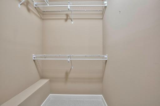 Lower-level walk-in closet with dual shelves and neutral tone for easy organizing.