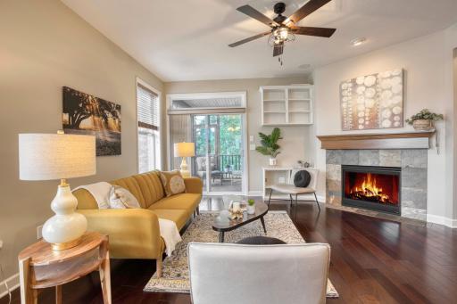 Cozy living space with a stone surround gas fireplace, custom built-ins, and sliding glass doors leading to the deck with wooded views.