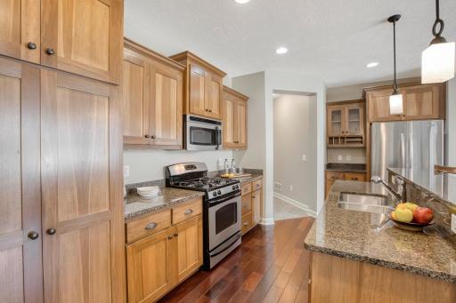 Stylish kitchen features granite countertops, a breakfast bar with pendant lighting, stainless steel appliances, and natural wood cabinetry.