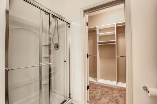 Glass-enclosed shower and convenient entry into the expansive walk-in closet with built-in shelving.