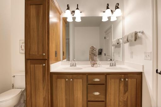 Bright and inviting bathroom featuring a dual-sink vanity with rich wood cabinetry, ample storage, and updated fixtures beneath elegant lighting.