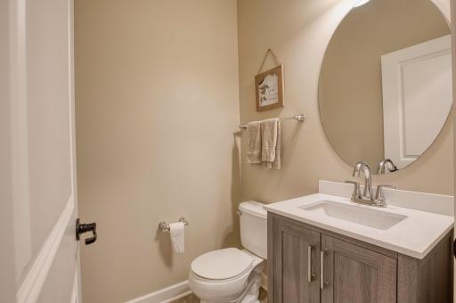 Conveniently located on the main level, this stylish half bath features a modern vanity with quartz countertop, brushed nickel fixtures, and a large round mirror for a clean, contemporary look.