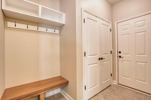 Practical and organized, this mudroom offers a built-in bench with cubby storage and coat hooks, double-door closet, and direct access to the garageâideal for keeping everyday essentials neatly tucked away.