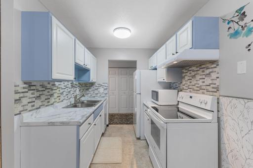 The galley style kitchen boasts crisp white cabinetry with a stylish backsplash and marbled countertops.