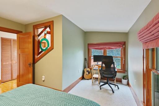 upper-level guest bedroom featuring a cozy desk nook with large windows, perfect for work or study. Accented with natural wood trim and a unique stained-glass detail for added character.