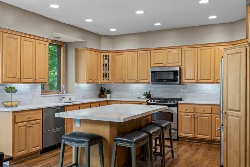The kitchen combines style and function with stainless steel appliances, new countertops, a porcelain-topped center island with breakfast bar seating, updated plumbing, and a tile backsplash.