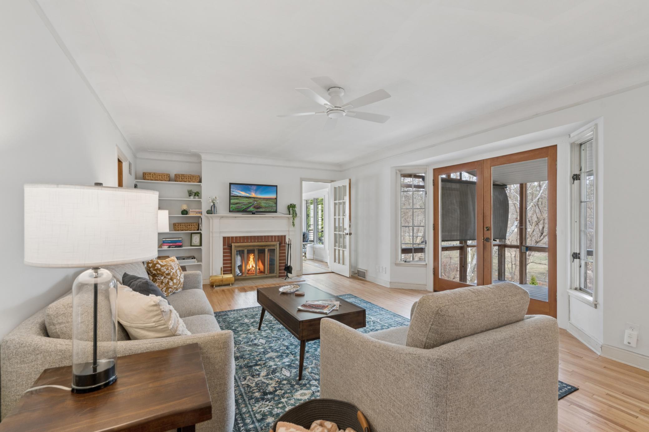 Bright and inviting living room with refinished hardwood floors, classic fireplace, and direct access to the screened porch overlooking Minnehaha Creek.