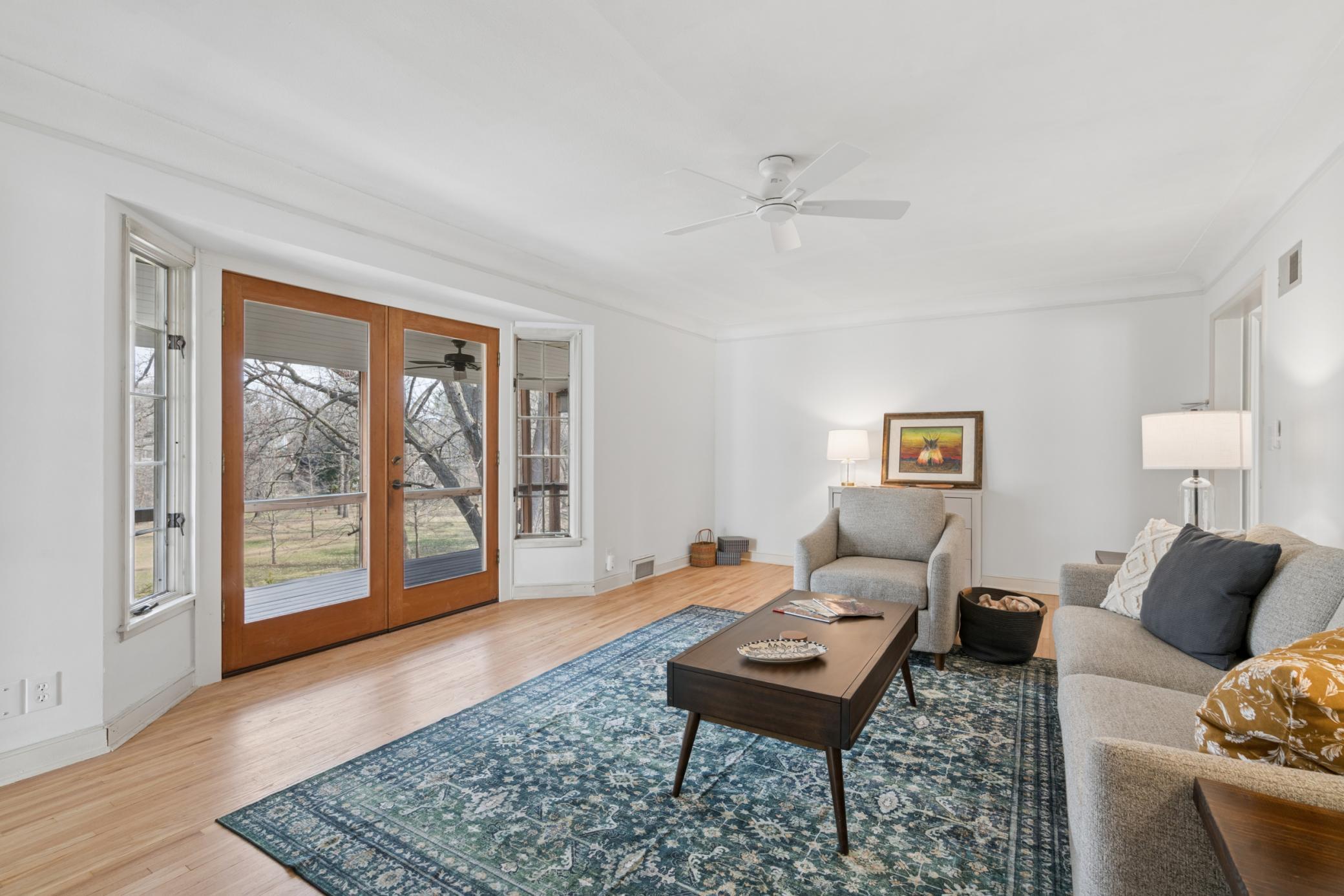 Expansive living room with oversized windows and French doors opening to a screened porch, creating a seamless connection to the private, creekside setting.