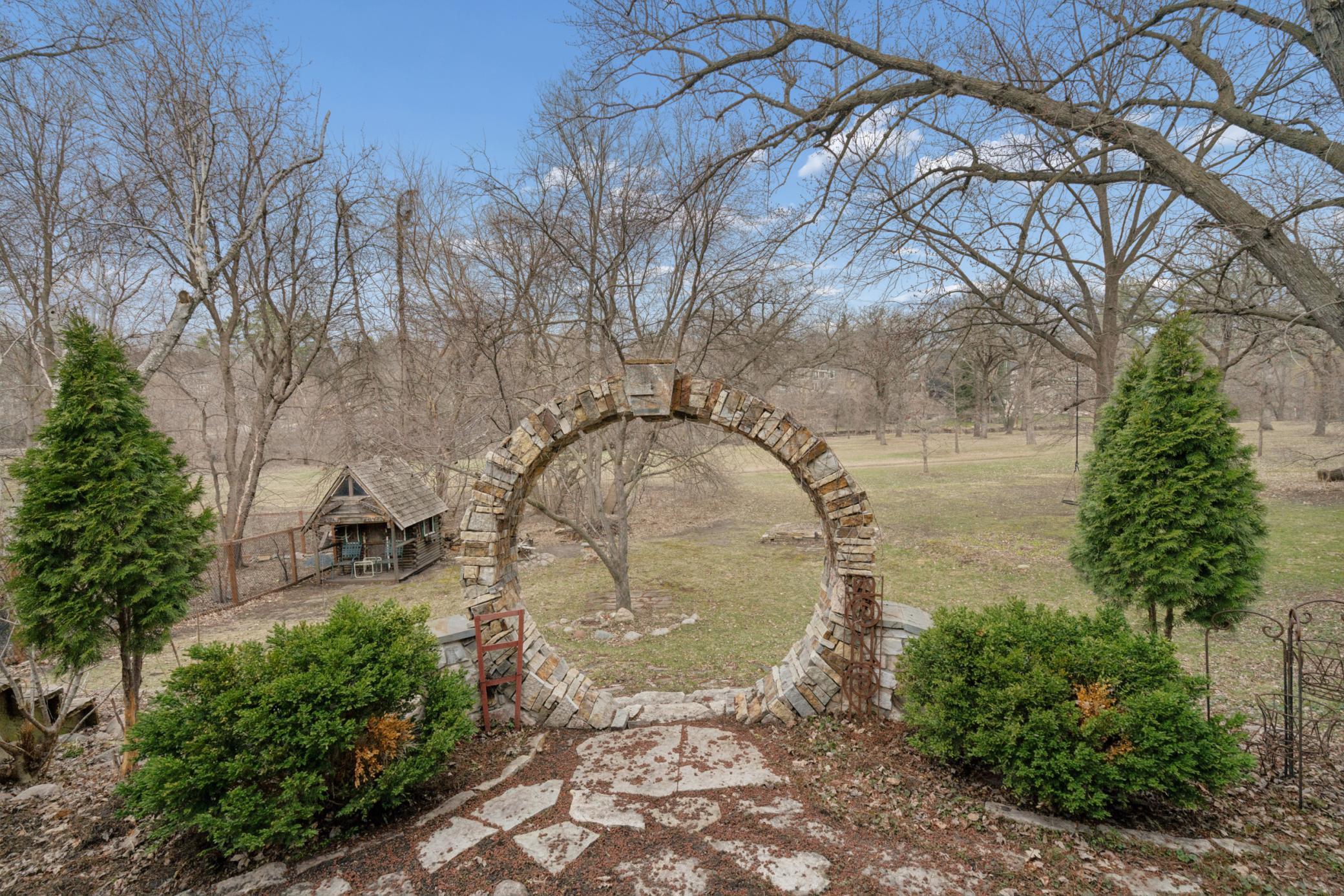 Charming stone archway creates a storybook entrance into the backyard and creekside setting