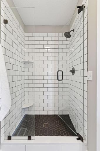 Large walk-in shower with newer tile surround and flooring as well as shampoo shelves and leg shaving ledge.