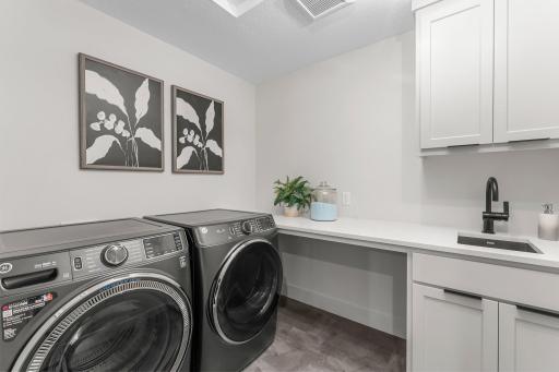A conveniently located laundry room with front-loading washer and dryer, utility sink, cabinetry, and counter space completes the upper level.