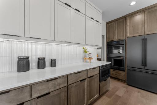 The space is elevated with elegant tile backsplash, stylish two-tone cabinetry, and under-cabinet lighting.