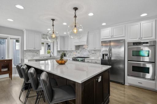 You'll find a large center island with custom soft-close cabinetry, quartz countertops, dual wall ovens, stainless steel appliances, and a generous pantry closet.