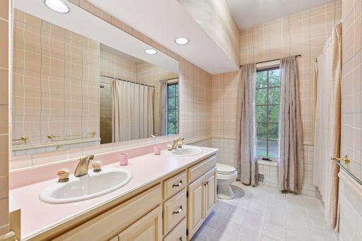 Full bathroom on the upper level with double sinks, tile flooring, and tub/shower.