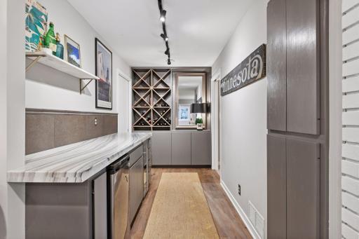 Stylish lower-level bar area with custom cabinetry, wine fridge, wine storage, and display shelving