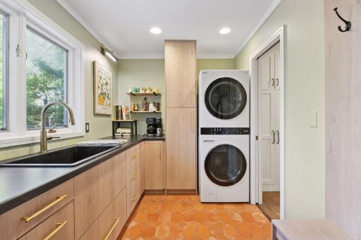 Stylish mudroom/laundry with stacked washer and dryer, sink, custom cabinetry, and ample counter space