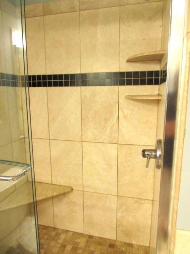 Step-in shower with shampoo shelves, cool stone floor and ceramic walls.