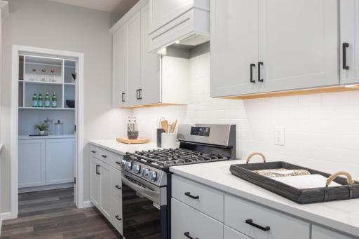 This kitchen features an upgraded slide-in gas range, seamlessly integrated with a stylish wood hood. The ceramic tile backsplash adds a modern touch. Photos are from previously built home; options and features may vary.