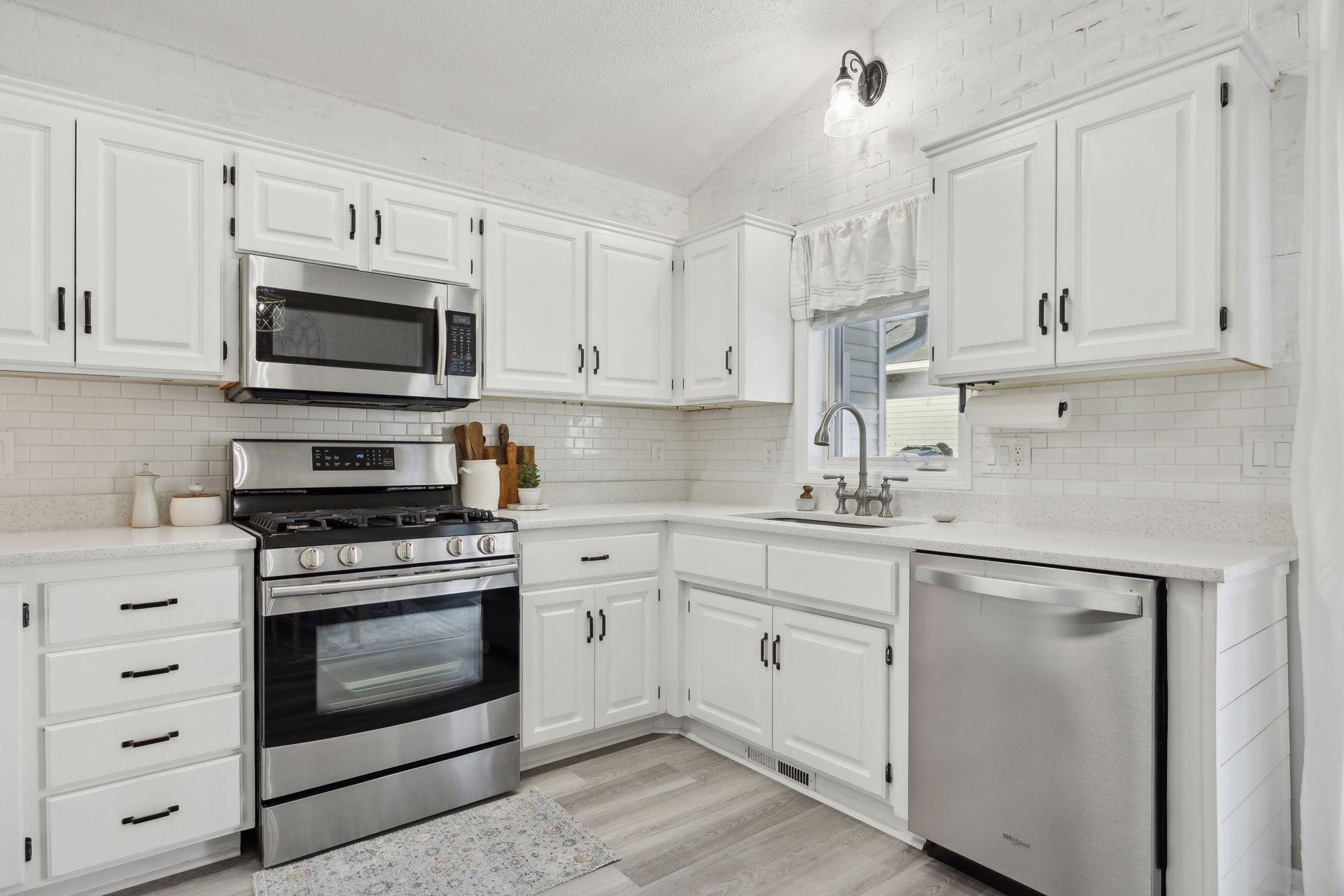 16x12 Main Level Kitchen updated with refaced white cabinetry in 2020, New dishwasher in 2024, new quartz countertops and backsplash, Fresh paint, new flooring, and white trim. North-facing windows and a sliding glass door to the side yard.