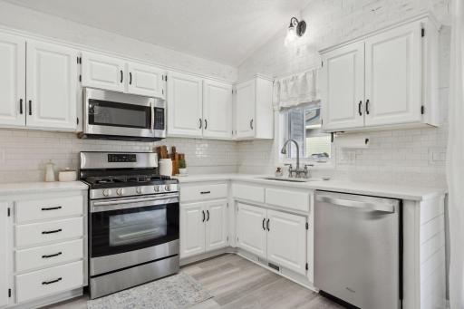 16x12 Main Level Kitchen updated with refaced white cabinetry in 2020, New dishwasher in 2024, new quartz countertops and backsplash, Fresh paint, new flooring, and white trim. North-facing windows and a sliding glass door to the side yard.