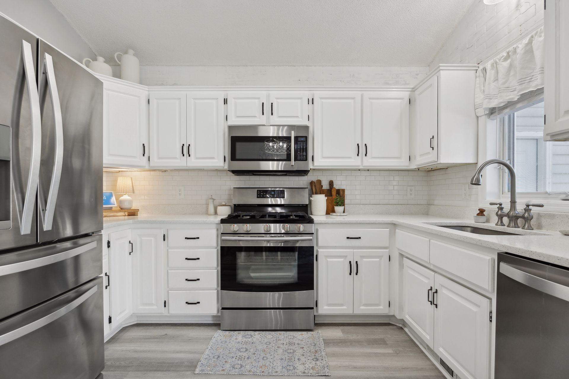 16x12 Main Level Kitchen updated with refaced white cabinetry in 2020, New dishwasher in 2024, new quartz countertops and backsplash, Fresh paint, new flooring, and white trim. North-facing windows and a sliding glass door to the side yard.